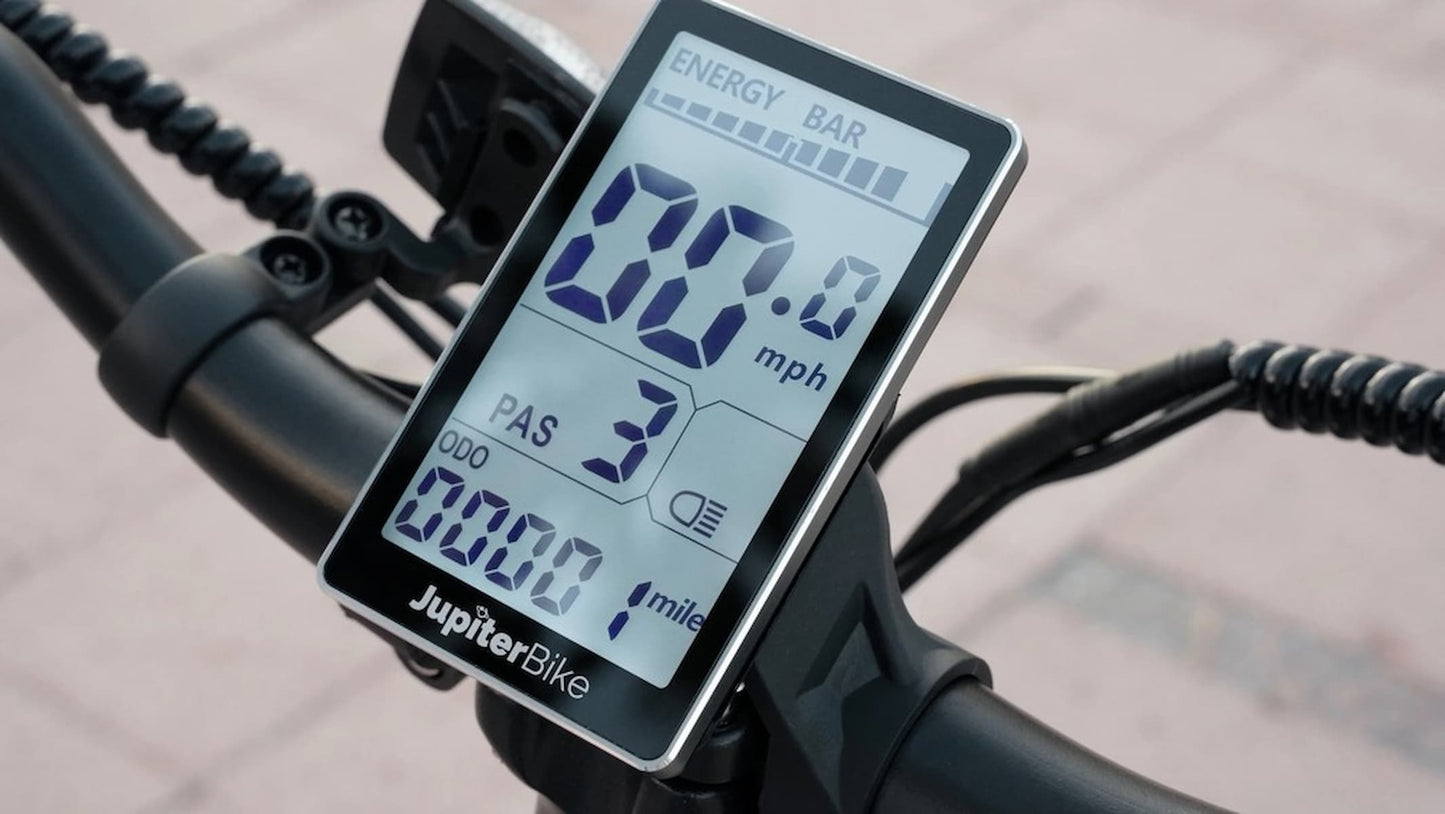 JupiterBikes Cruise Electric Bike – A close-up of a JupiterBike digital display mounted on a bicycle handlebar, showing speed, battery percentage, and other cycling metrics.