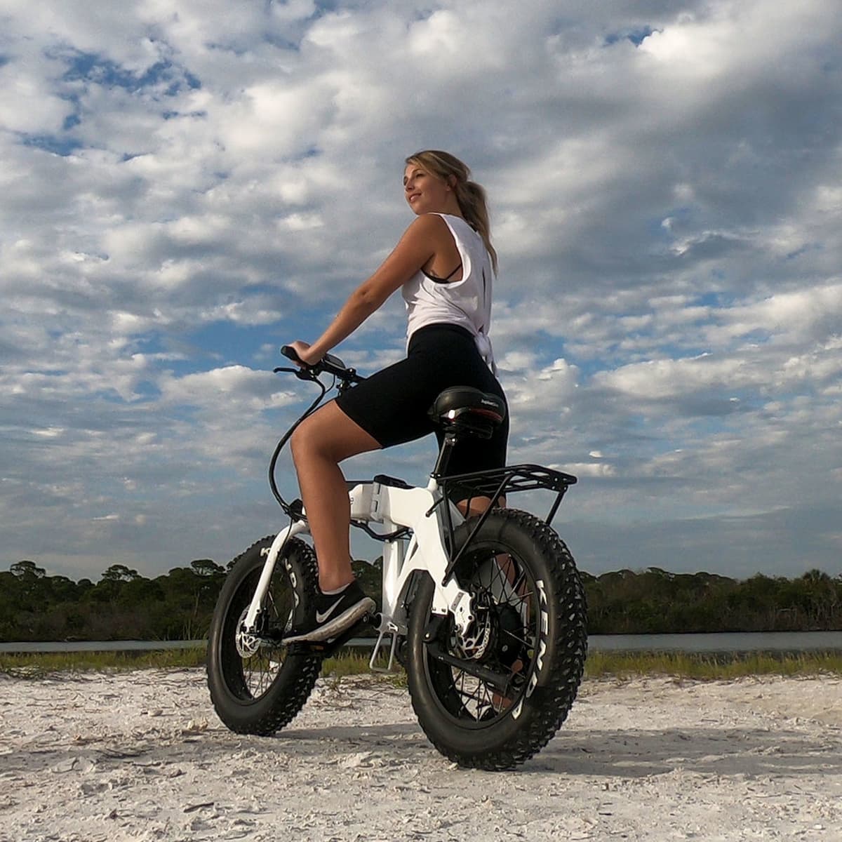 JupiterBikes_Young lady riding a fat-tire e-bike called Defiant on a dirt/sandy path with a cloudy sky in the background