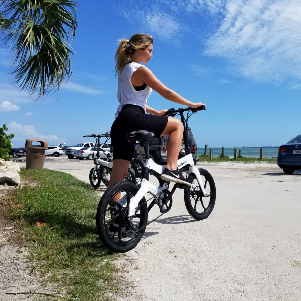 Jupiter_Discovery x7_Woman riding a white electric bike on a road near beach with cars and palm trees in the background