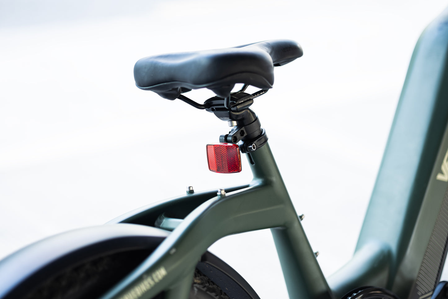 velowave_Close-up of a Green Pony electric bicycle seat and frame with a red taillight on a blurred background