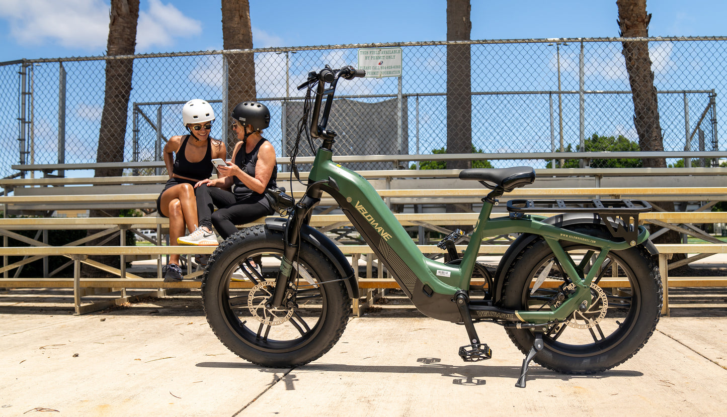 velowave_Two people sitting on a bench with a green Pony electric bike in front of them.