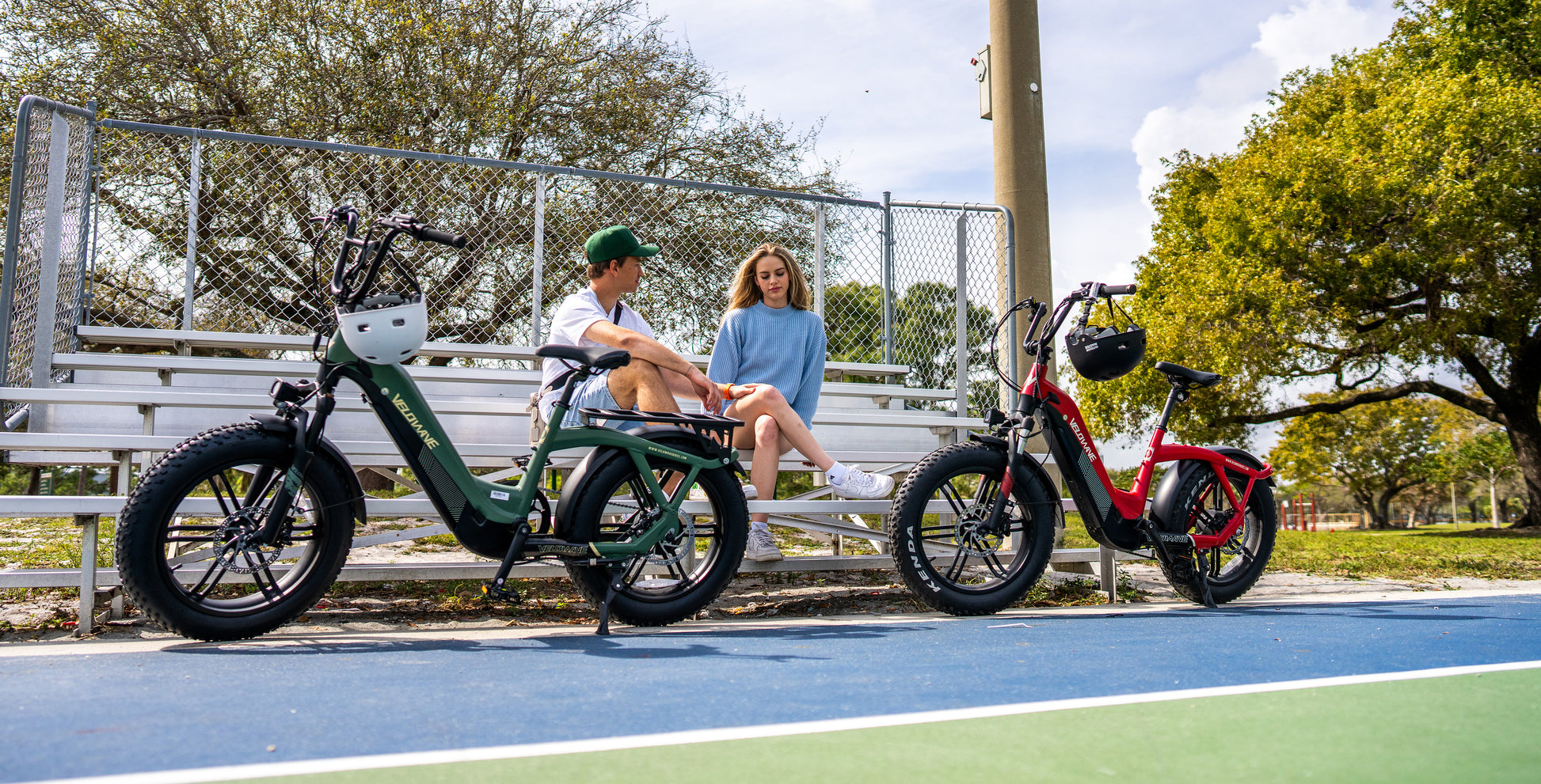 velowave_Two Pony electric bikes on a basketball court with people sitting on a bench.