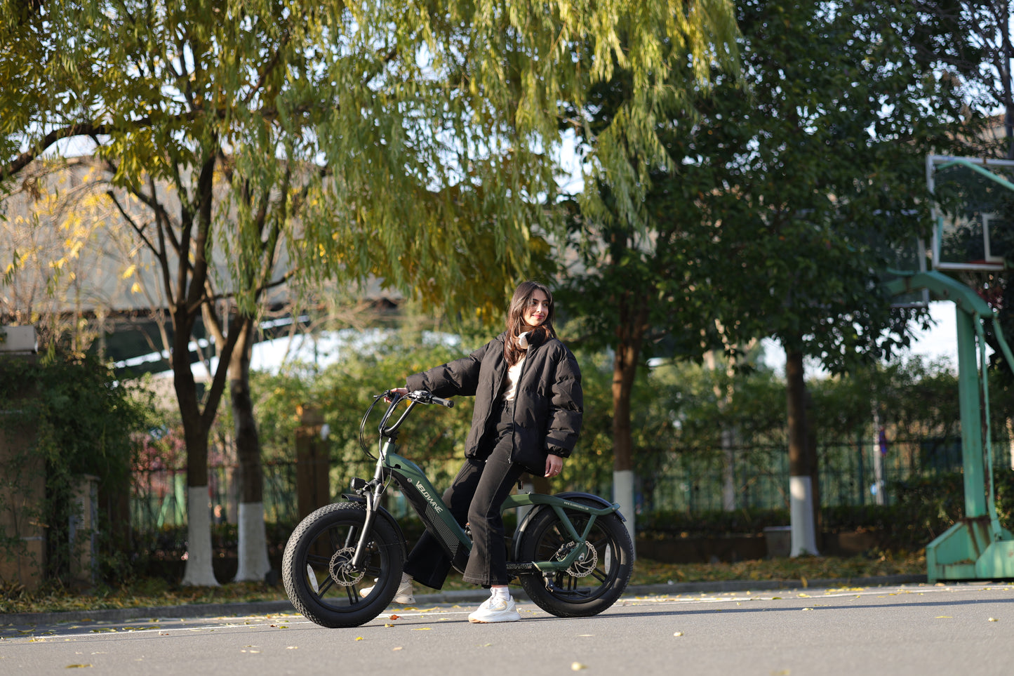 velowave_Person riding a Pony electric bicycle in an urban park setting with trees and buildings in the background.