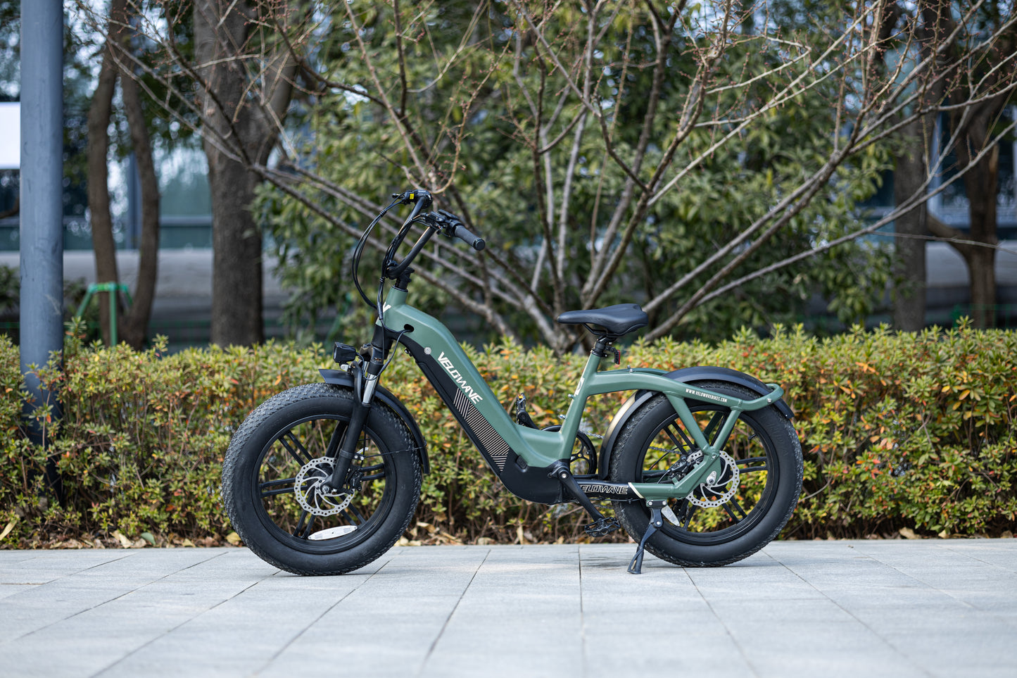 velowave_Green electric bike parked on a sidewalk with trees and bushes in the background – Pony